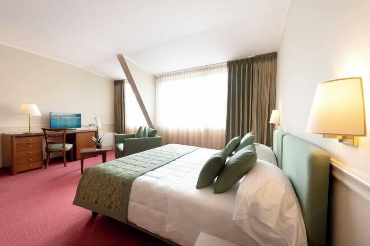 Une chambre d’hôtel avec un lit, un bureau, une chaise, une lampe et un tableau au mur.