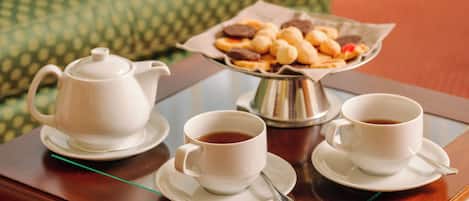 A table with a teapot, two cups of coffee, and a tray of pastries in a hotel room.