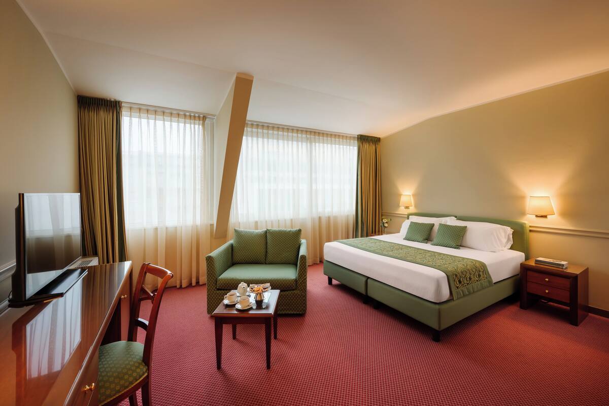 Une chambre d’hôtel avec un lit, un bureau, une chaise, une télévision et une table avec une tasse et une soucoupe.