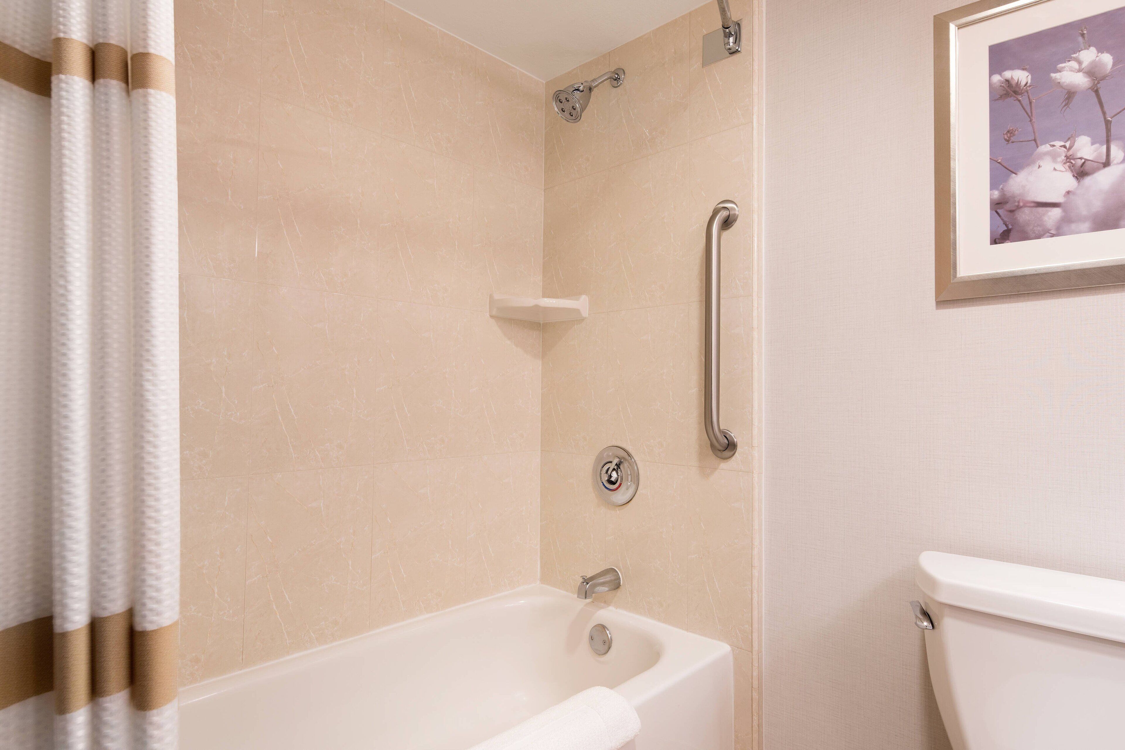 Un baño con bañera, inodoro y ducha con barra de apoyo.
