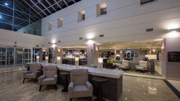 A spacious lobby with a high ceiling, a central bar area, seating arrangements, and a glass facade. - Bakersfield Marriott at the Convention Center (Bakersfield)