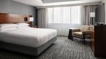 A hotel room with a large bed, a desk, a chair, a TV, and a window with curtains.