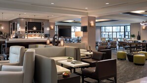 A modern hotel lobby with seating areas, a bar, and a large TV screen. - Bakersfield Marriott at the Convention Center (Bakersfield)