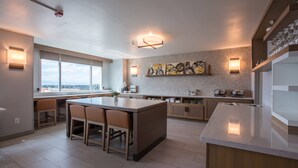 A modern kitchen with a central island, bar stools, and a view of the city through large windows. - Bakersfield Marriott at the Convention Center (Bakersfield)