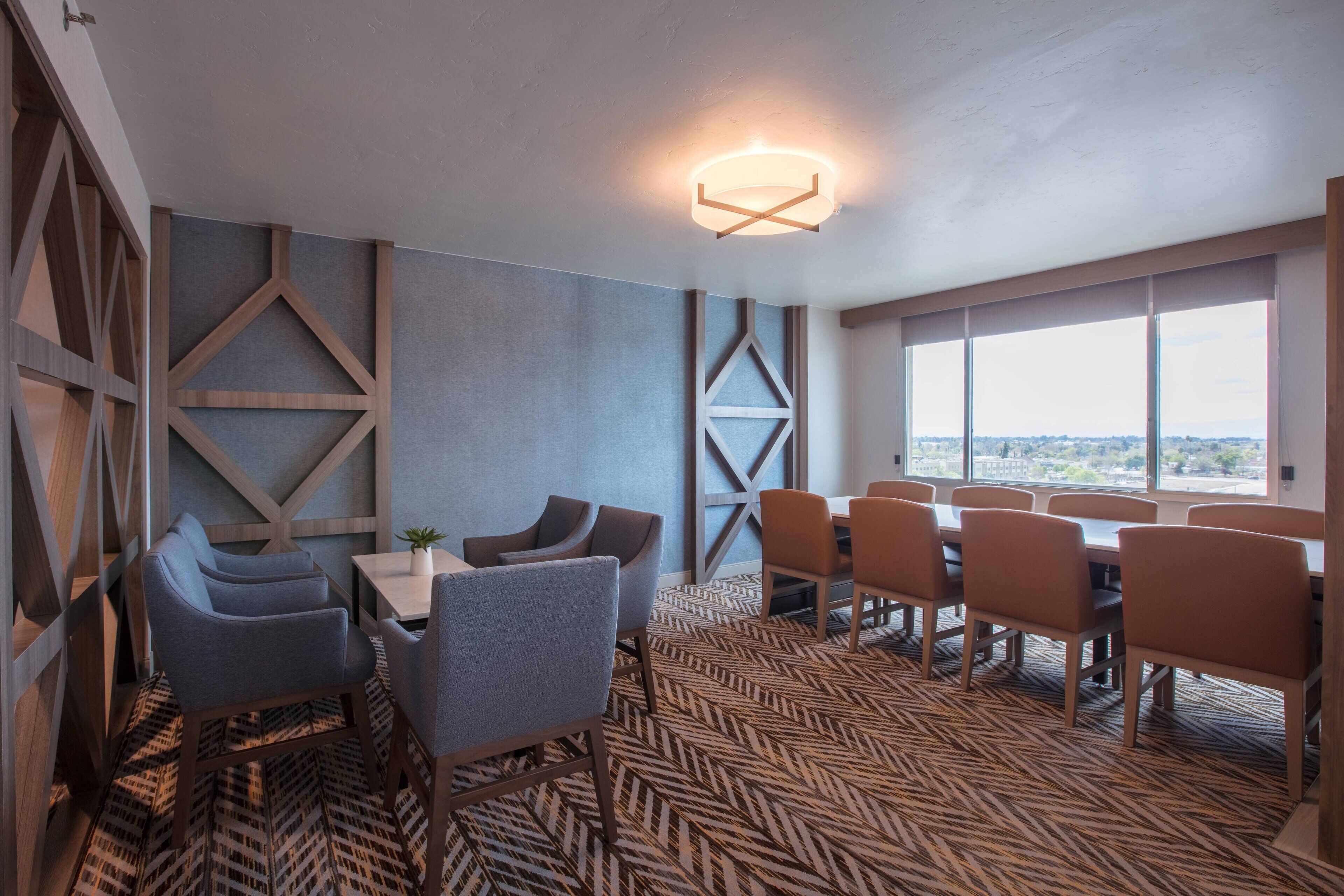 Un comedor moderno con una mesa grande y sillas, patrones geométricos en la pared y vistas amplias a través de grandes ventanales.
