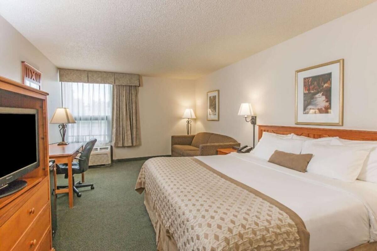 A hotel room with a bed, desk, chair, television, and two wall-mounted lamps.