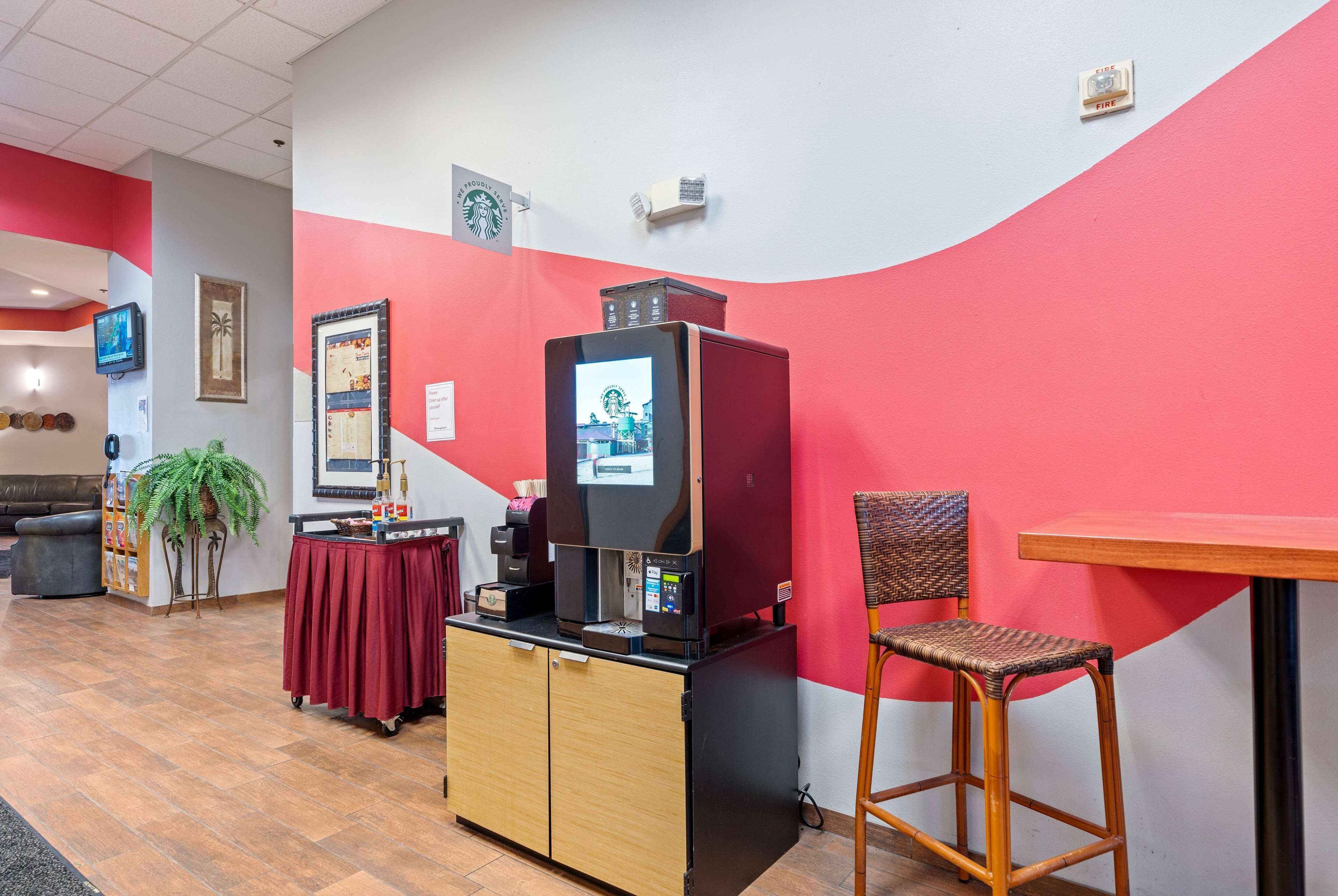 Een moderne kamer met een rode en witte wand, een koffieapparaat, een klein tafeltje, een rieten stoel en een televisie op een standaard.