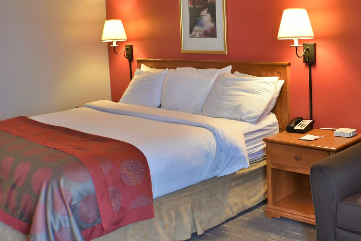 A hotel room with a bed, two bedside lamps, a nightstand with a phone, a chair, and a framed picture on the wall.