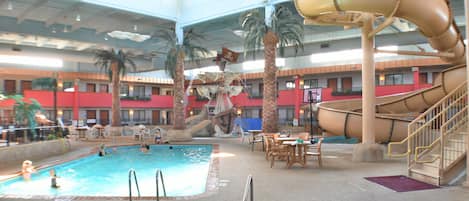 Una piscina interior con tobogán, palmeras y un jacuzzi.