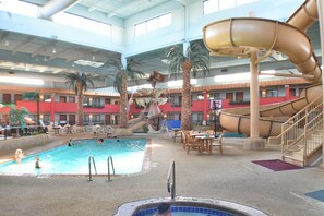 Una piscina al coperto con scivolo, palme e vasca idromassaggio.