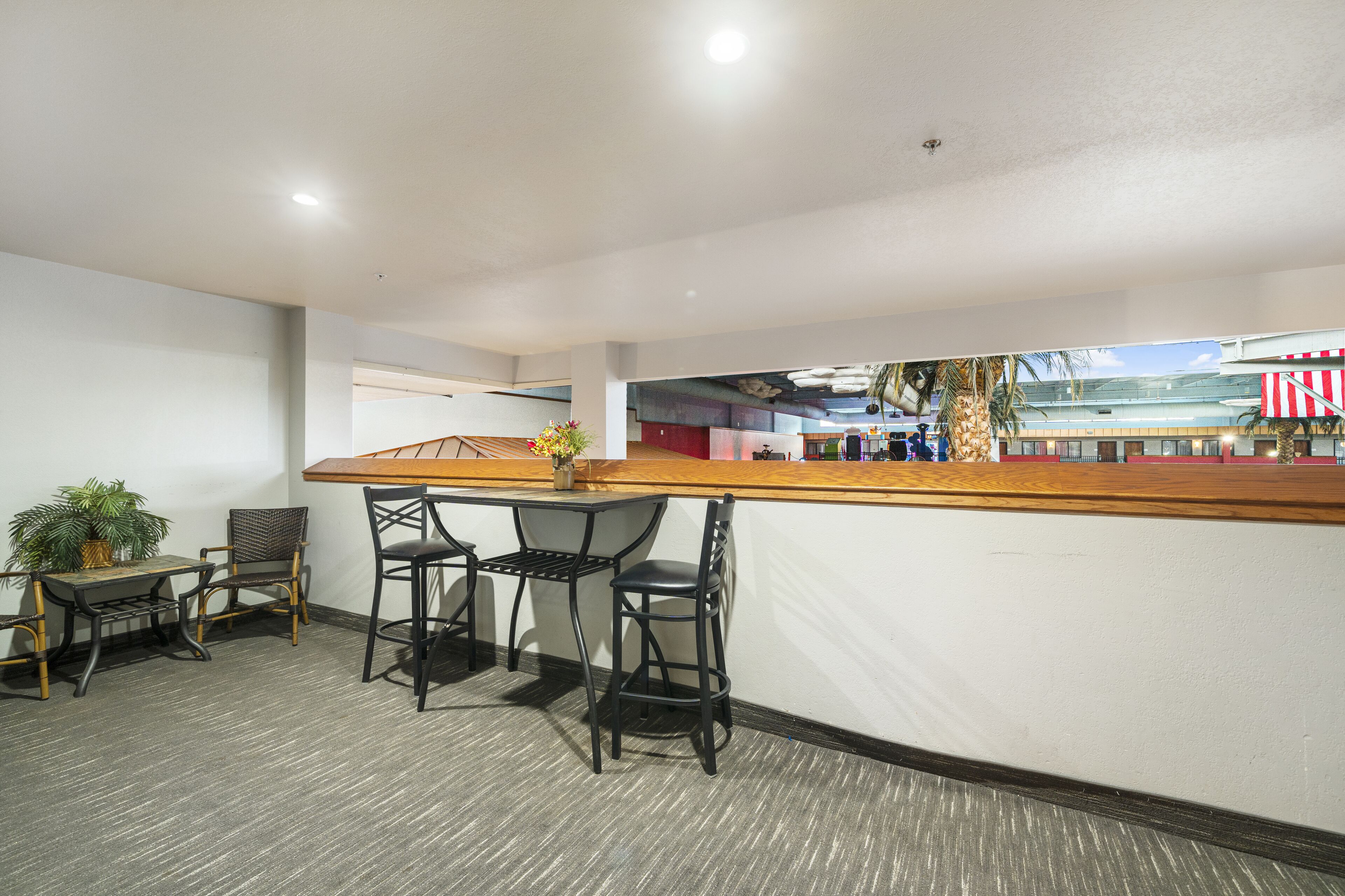 A bar area with a wooden counter, three black chairs, and a small table with a potted plant.