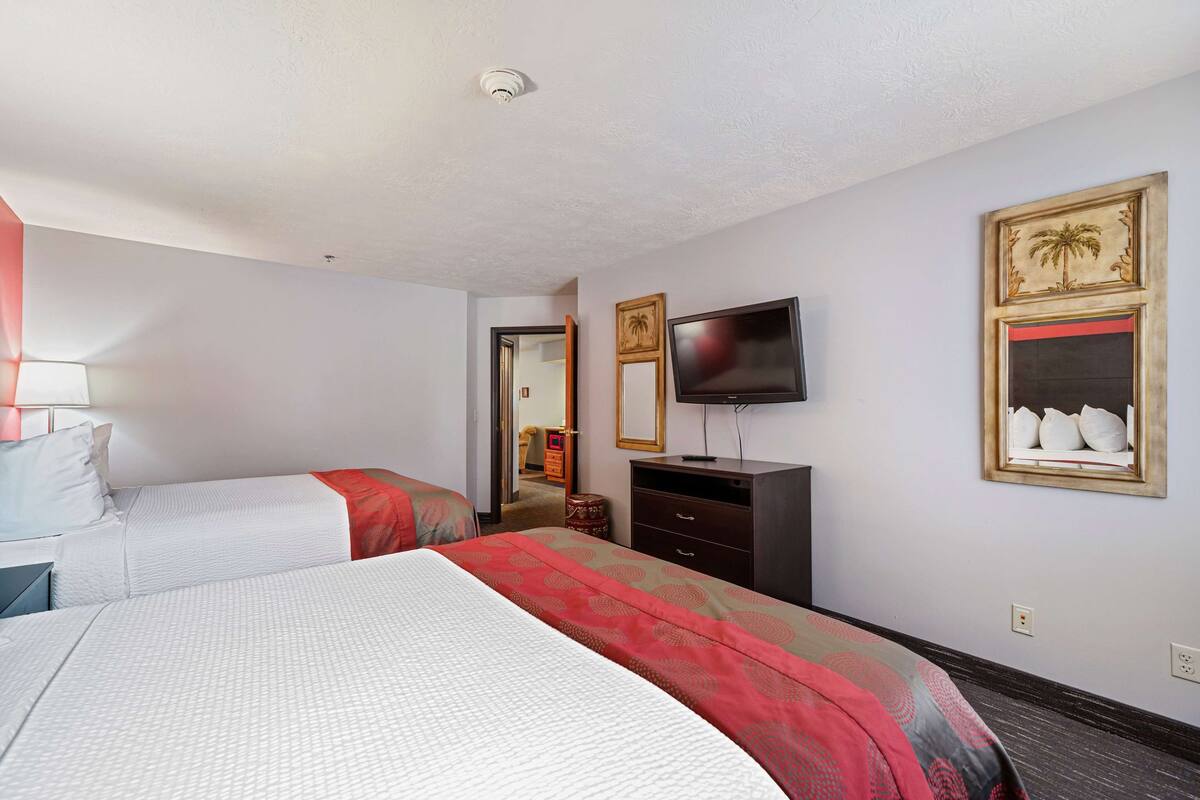 A hotel room with two beds, a TV, a dresser, and a mirror.