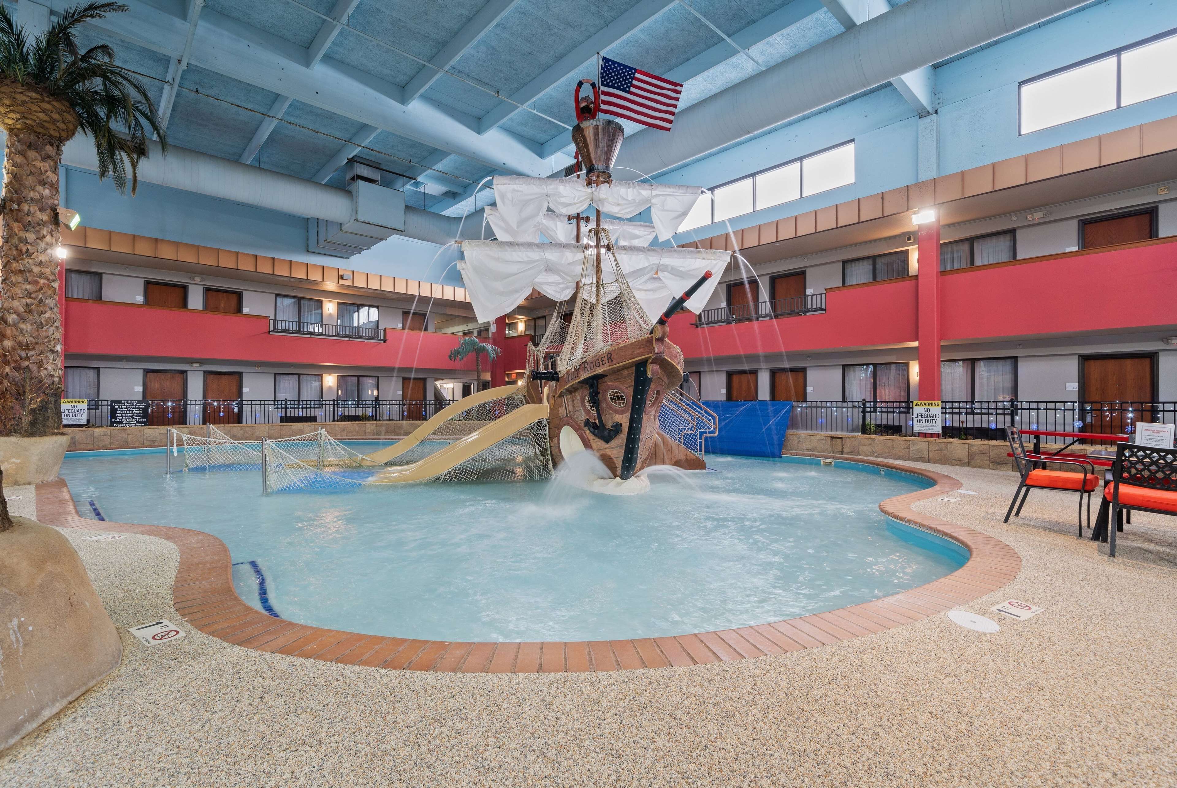 An indoor swimming pool with a pirate ship decoration, surrounded by a multi-level building with balconies.