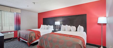 Une chambre d’hôtel avec deux lits, une grande tête de lit sombre, un bureau et une lampe sur pied.