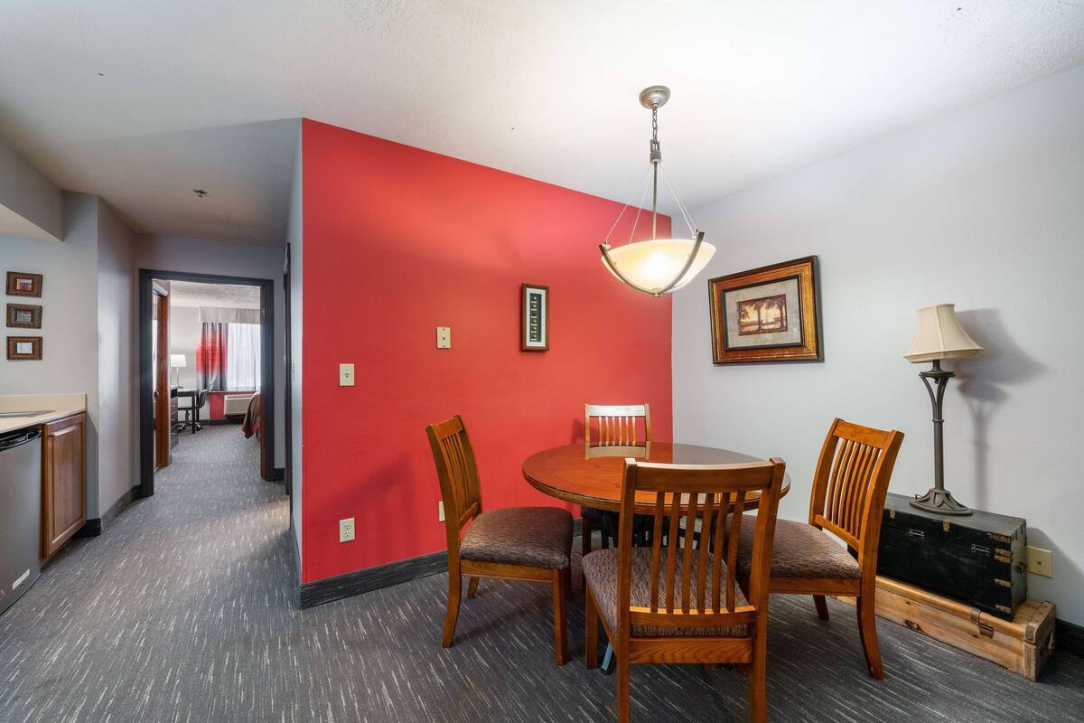 A dining area with a round table, wooden chairs, a hanging light fixture, and a lamp on the wall.