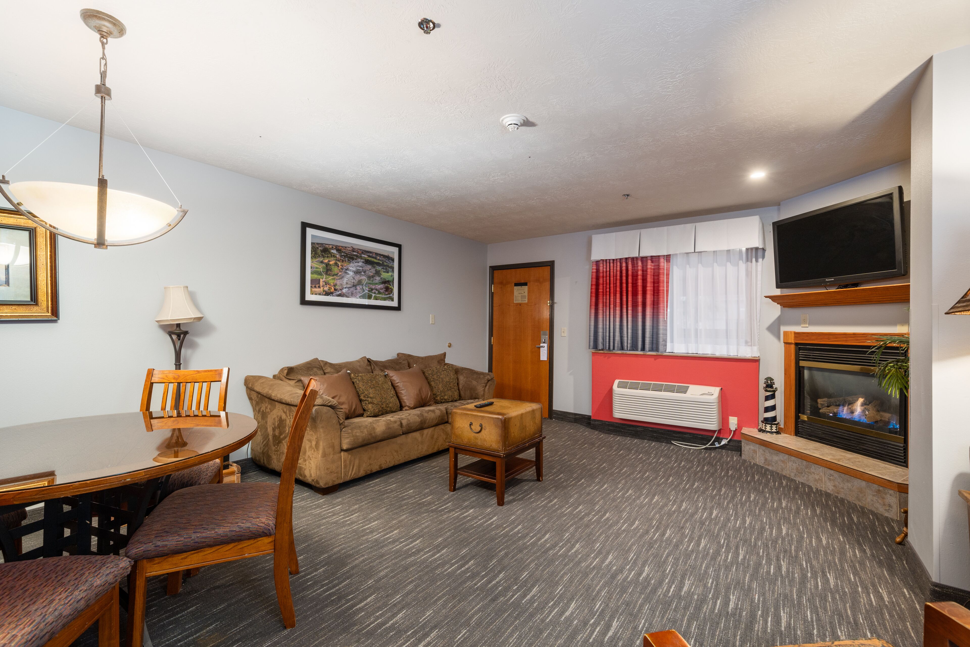 A living room with a sofa, a dining table with chairs, a television mounted on the wall, and a fireplace.