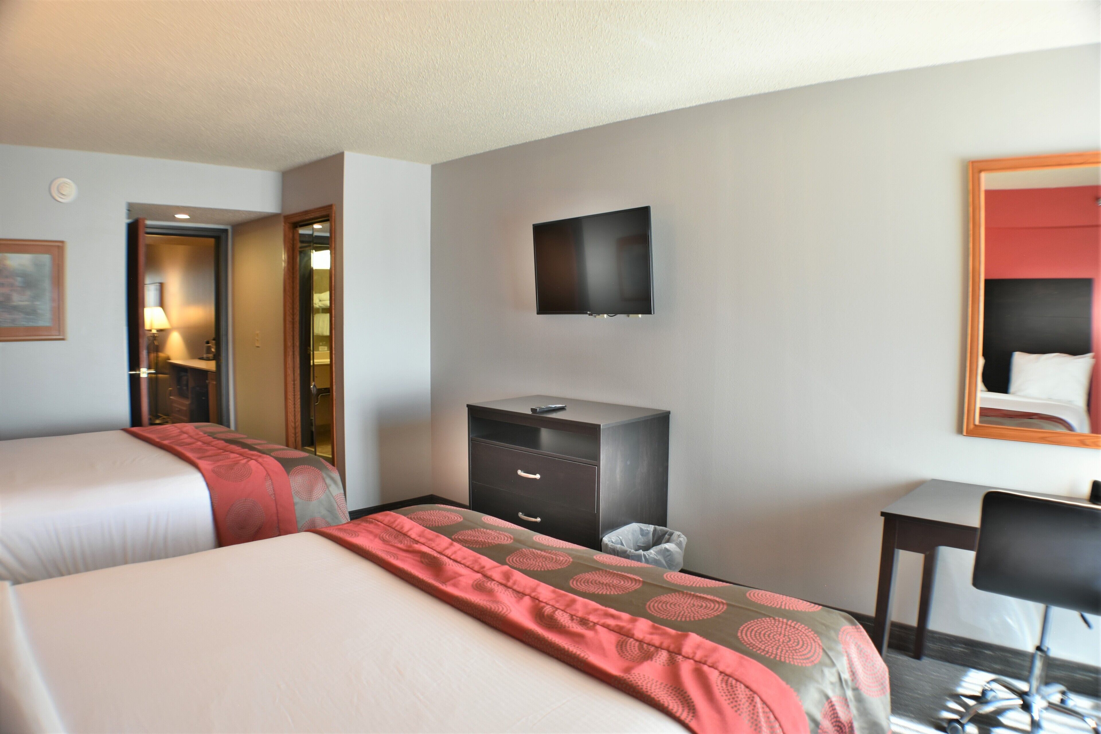 A hotel room with two beds, a TV mounted on the wall, a desk, and a chair.