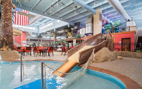 An indoor pool area with a slide, seating, and tropical decor.