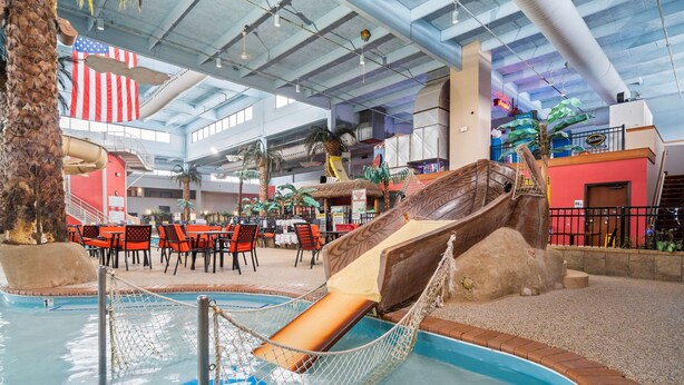 Un espace piscine intérieure doté d’un toboggan, de sièges et d’une décoration de style tropical.
