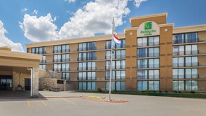 A Holiday Inn Express building with a stone facade, multiple balconies, and a flagpole with flags. - Holiday Inn Hotel & Suites Des Moines - Northwest by IHG (Urbandale)
