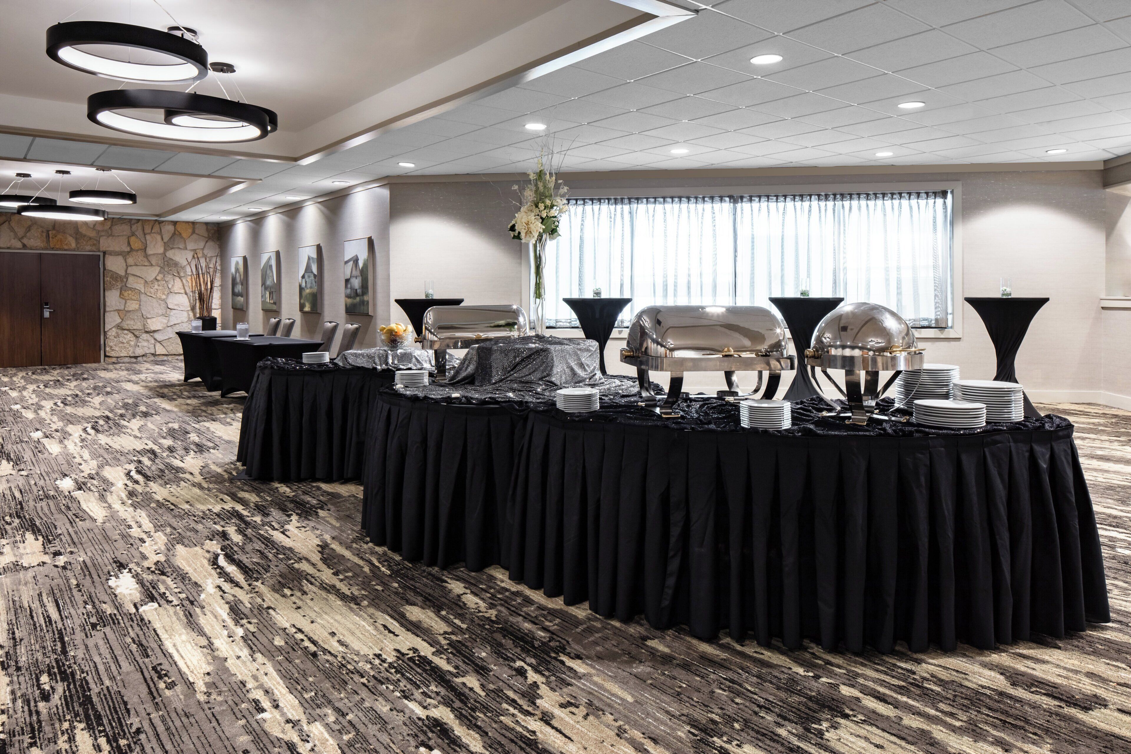 A conference room with a long table set for a meeting, surrounded by chairs, with a stone wall and a large window in the background.