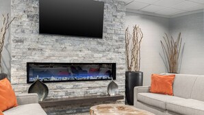 Een moderne woonkamer met een stenen openhaard, een flatscreen televisie en een grijze bank met oranje kussens.