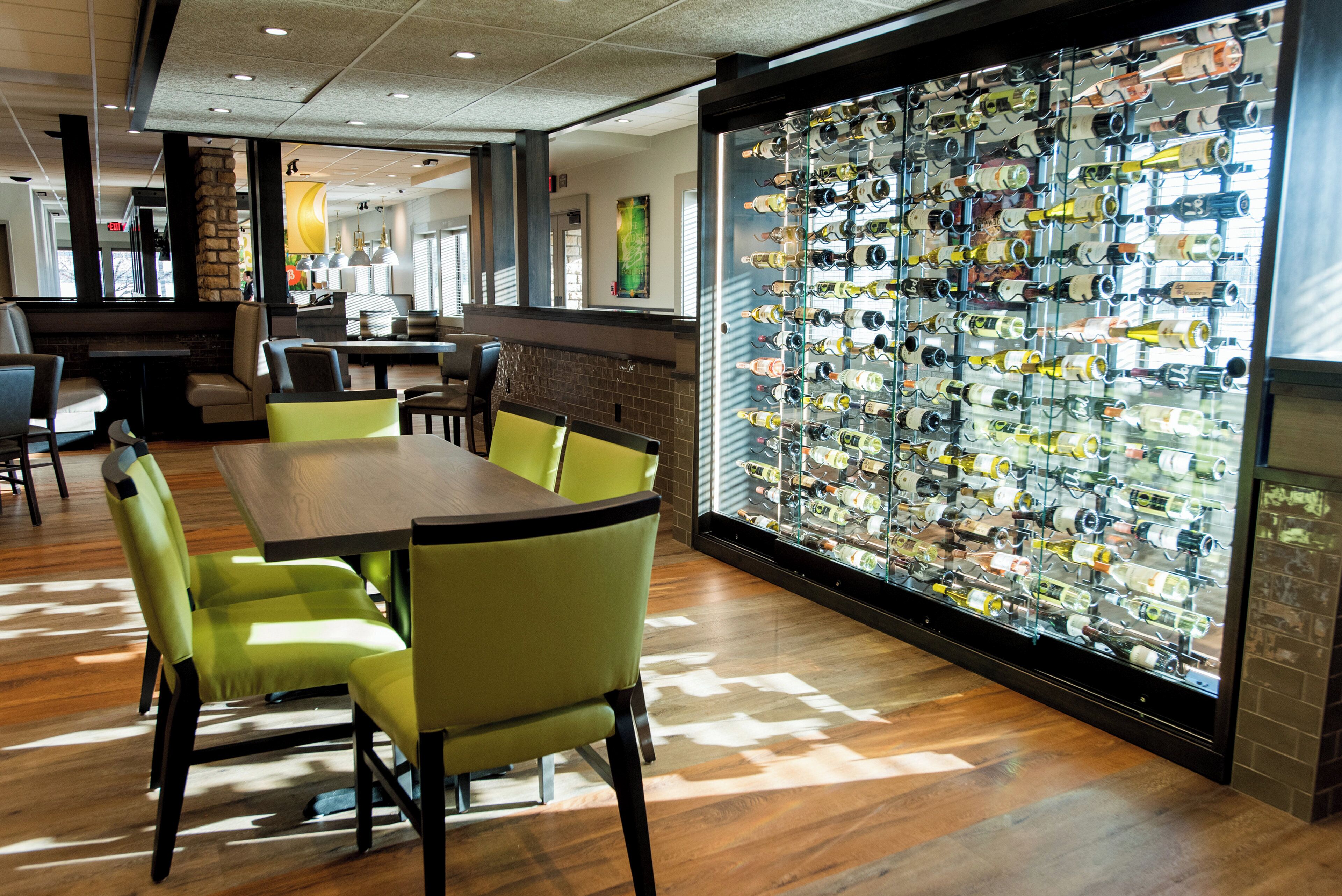 Un restaurante con una mesa larga y sillas, una estantería con varias botellas de vino y una pared de ladrillo.