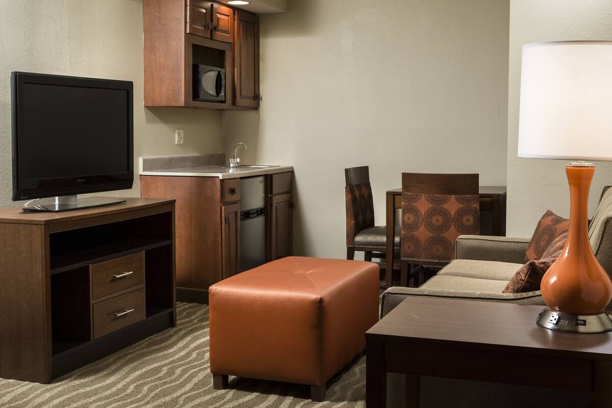 Une chambre d’hôtel compacte comprenant un coin cuisine, un téléviseur à écran plat, un canapé, une table basse et une lampe.