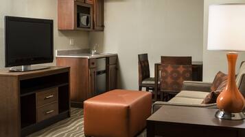 Una habitación de hotel compacta con kitchenette, un televisor de pantalla plana, un sofá, una mesa de centro y una lámpara.