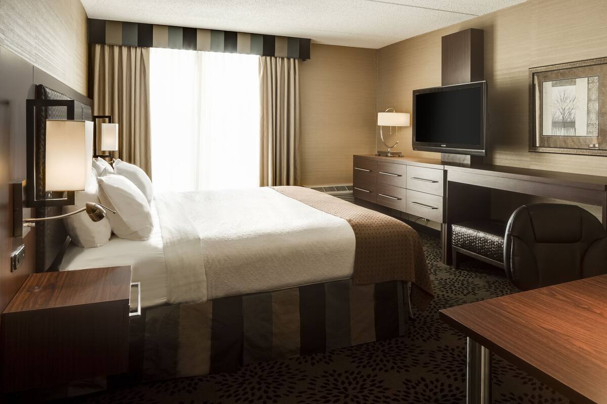Une chambre d’hôtel avec un grand lit, un bureau, une chaise, une télévision et une commode.