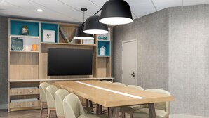 Een moderne vergaderruimte met een lange tafel, meerdere stoelen, een grote flatscreen-tv en ingebouwde planken met decoratieve objecten.
