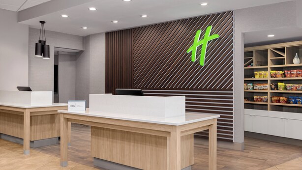 Een receptie met twee balies, een moderne lamp, een muur met een geometrisch patroon en een plank met snacks.