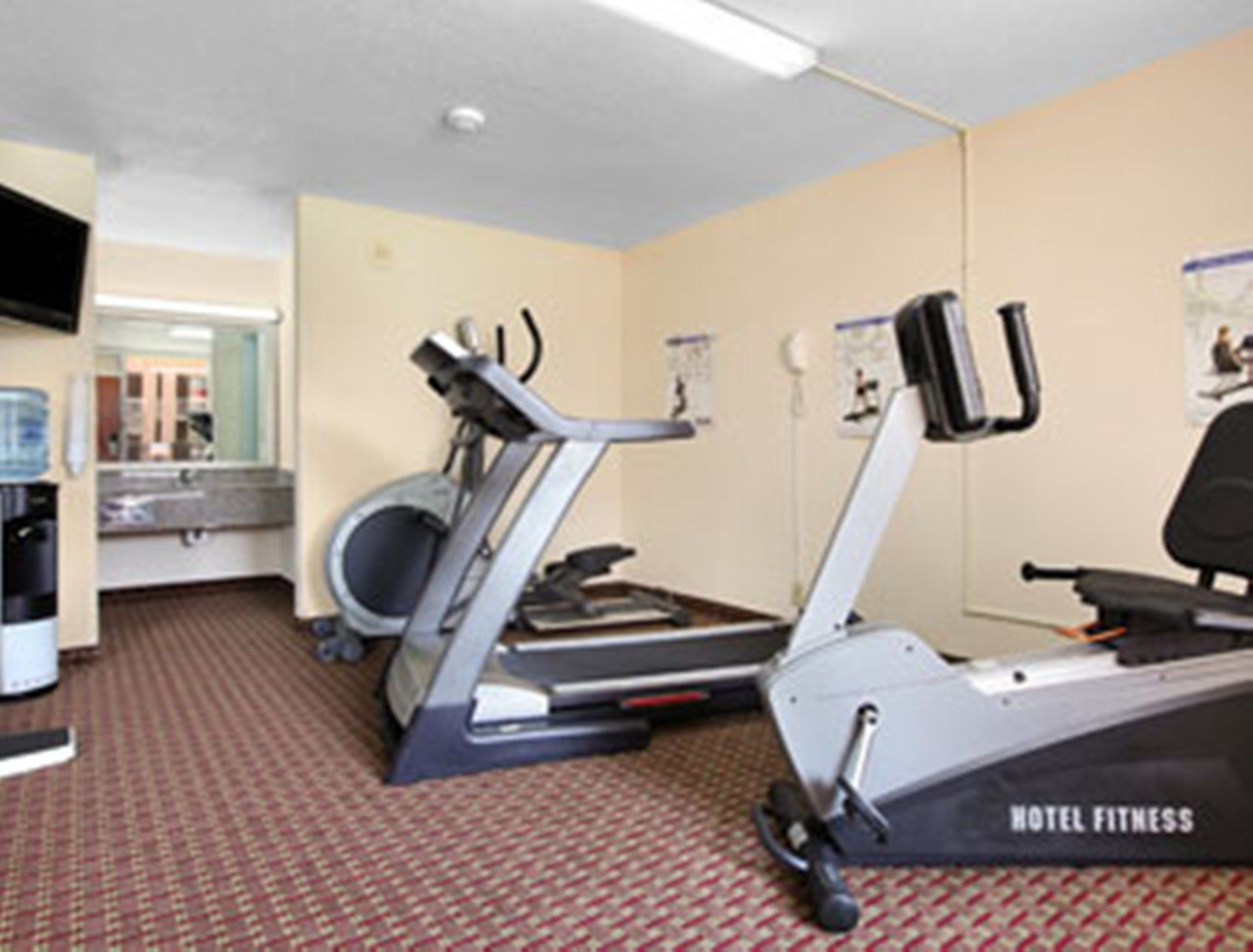 Gimnasio de hotel con equipo de ejercicio, dispensador de agua y un espejo.