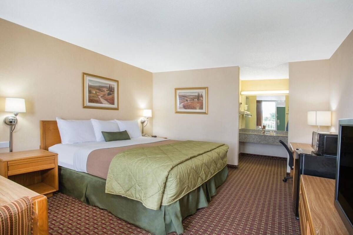 Une chambre d’hôtel comprenant un lit, des tables de chevet, un bureau, une chaise, un téléviseur et deux tableaux encadrés accrochés aux murs.