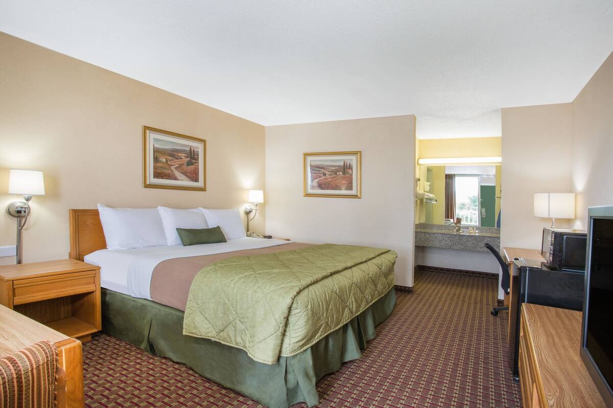 Une chambre d’hôtel comprenant un lit, des tables de chevet, un bureau, une télévision et deux tableaux encadrés accrochés aux murs.