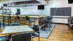 Uma área de bar moderna com um balcão extenso, vários bancos e um espaço de estar com mesas e cadeiras.