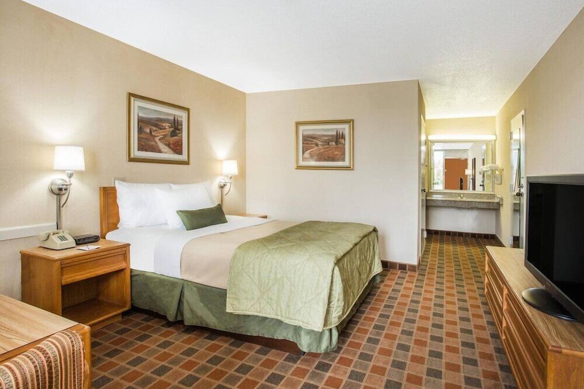 Une chambre d’hôtel avec un lit, des tables de chevet, une télévision et une salle de bain visible à travers une porte ouverte.