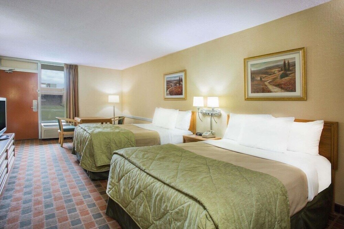 Une chambre d’hôtel avec deux lits, un bureau, une chaise, une télévision et deux tableaux accrochés au mur.