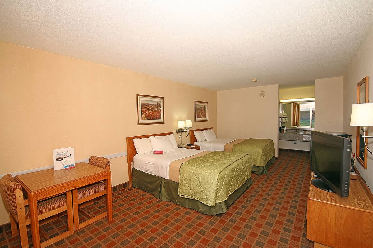 Une chambre d’hôtel avec deux lits, un bureau avec une chaise, une télévision et une petite table.