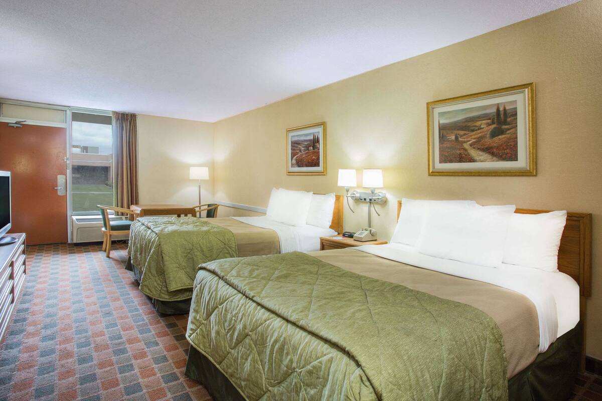 Une chambre d’hôtel avec deux lits, un bureau, une chaise, une télévision et deux tableaux au mur.