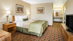 Quarto de hotel com cama, mesa de cabeceira com telefone, televisão e espelho.