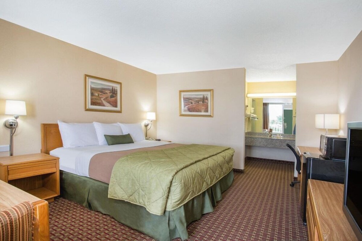 Une chambre d’hôtel comprenant un lit, des tables de chevet, un bureau, une chaise, un téléviseur et deux tableaux encadrés accrochés aux murs.
