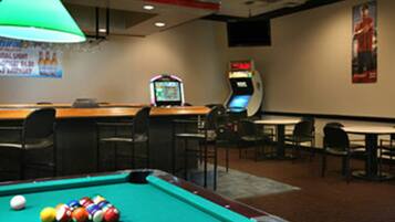 A pool table with balls, a green lamp, a bar area, and arcade machines.