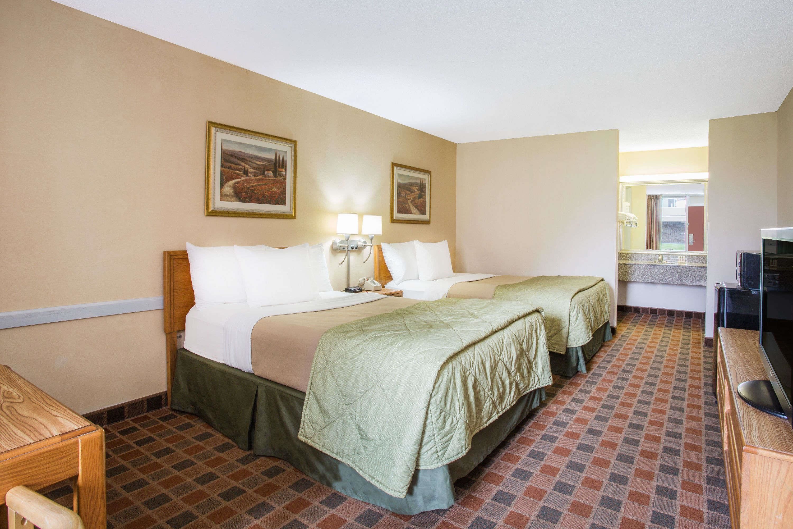 A hotel room with two beds, a desk, a TV, and a bathroom visible through an open door.