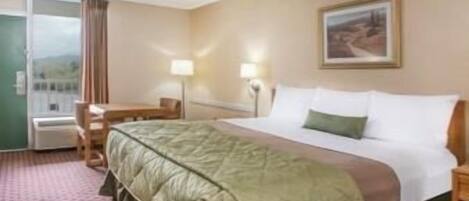 Quarto de hotel com cama, escrivaninha, cadeira, abajur e janela com cortinas.