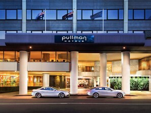 A hotel entrance with a sign reading 'Pullman Hotels,' two cars parked in front, and flags flying. - Pullman Sydney Hyde Park (Darlinghurst)