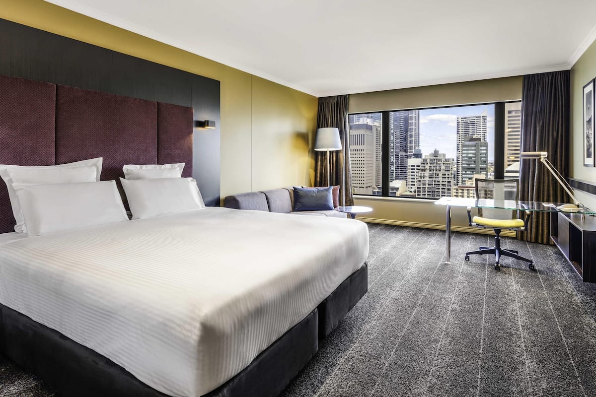Een hotelkamer met een groot bed, een bureau, een stoel en uitzicht op de stad.