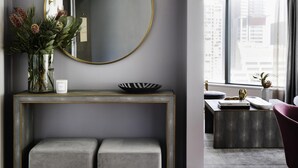 A modern room with a round mirror, a console table with a vase of flowers, and a view of the city through large windows. - Pullman Sydney Hyde Park (Darlinghurst)