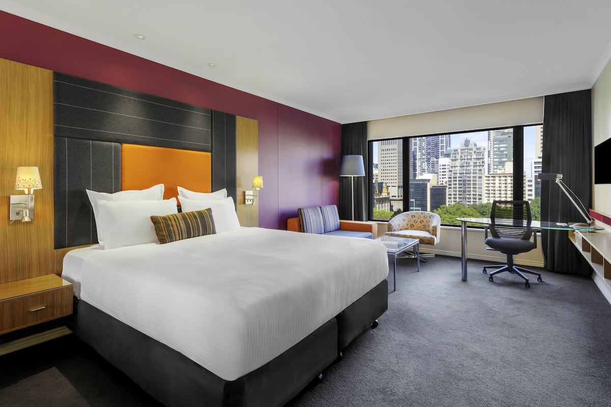 Een hotelkamer met een groot bed, een bureau, een stoel en uitzicht op de stadshemel.