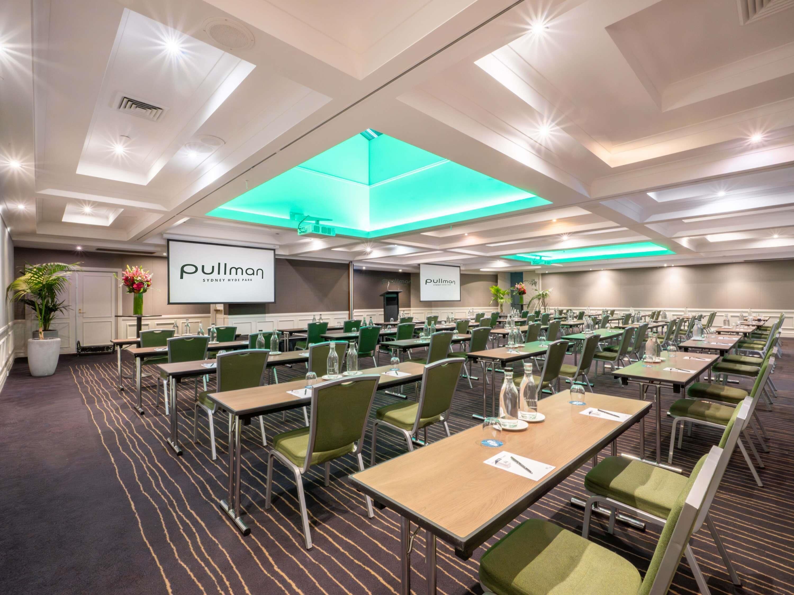 A conference room with tables, chairs, and a large screen displaying the Pullman logo.